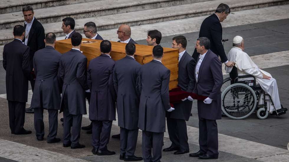 Papa Francisco a ser levado de cadeira de rodas enquanto o corpo de Bento XVI é levado para dentro da Basílica de S. Pedro