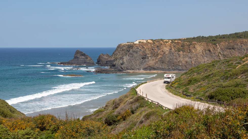 Motorhome parked at viewpoint of Atlantic Ocean waves breaking on rocky headland and bay with sandy beach, Praia de Odeceixe, Algarve, Portugal