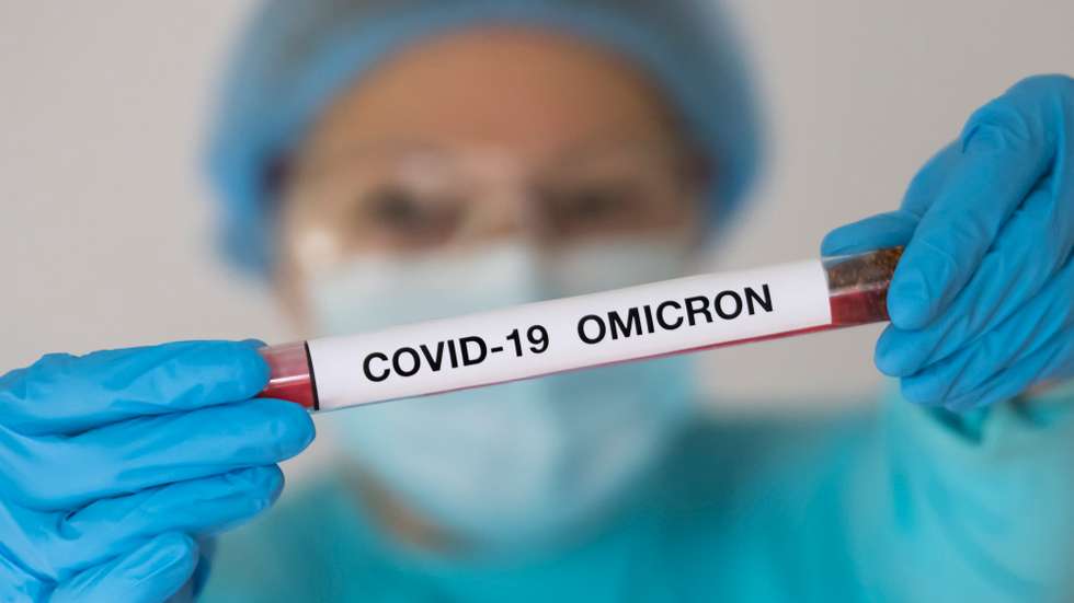 Uma mulher com um fato protetor uma máscara segura um tubo de testagem como uma amostra de um infetado com a variante Ómicron