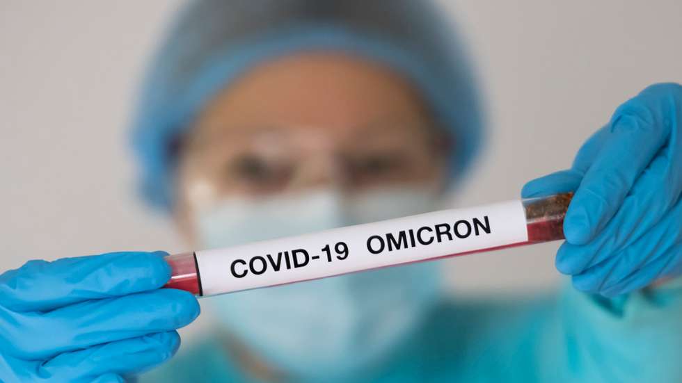 Uma mulher com um fato protetor uma máscara segura um tubo de testagem como uma amostra de um infetado com a variante Ómicron