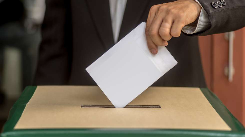 Hand of a person casting a vote into the ballot box during elections