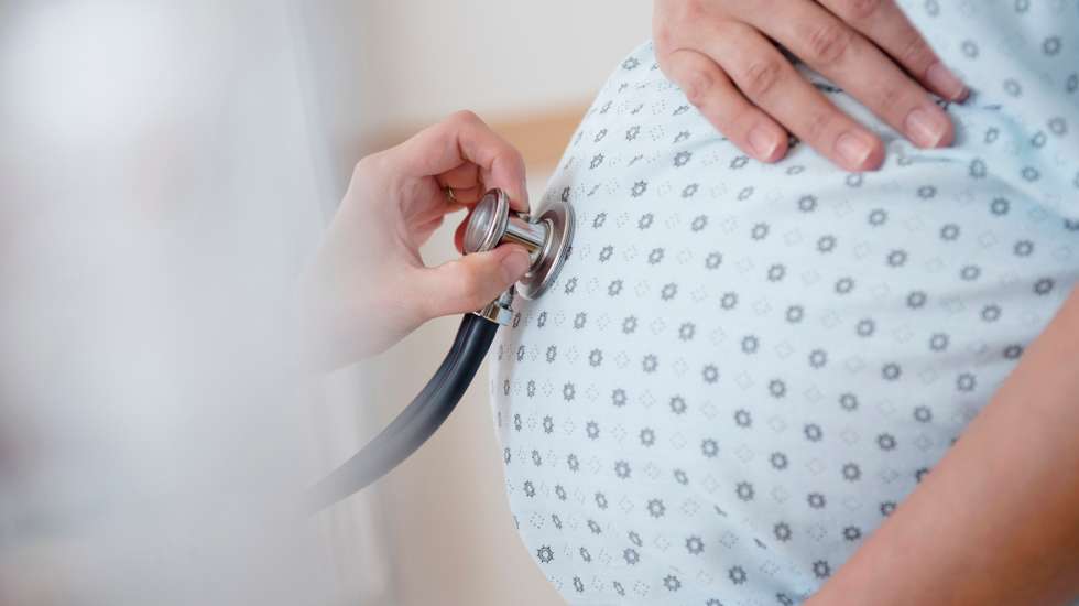 Doctor listening to belly of pregnant woman