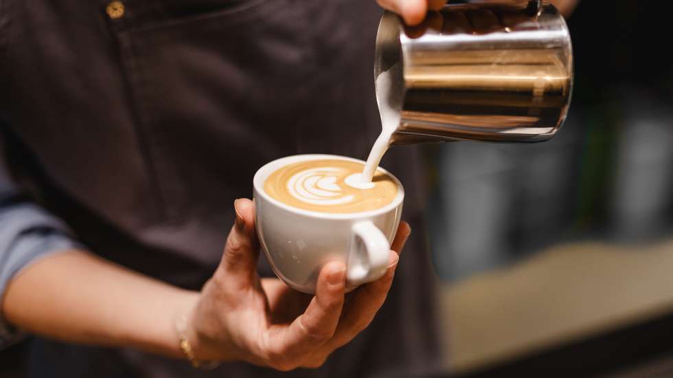 close up view of Young woman preparing a coffee by drawing a flower with milk