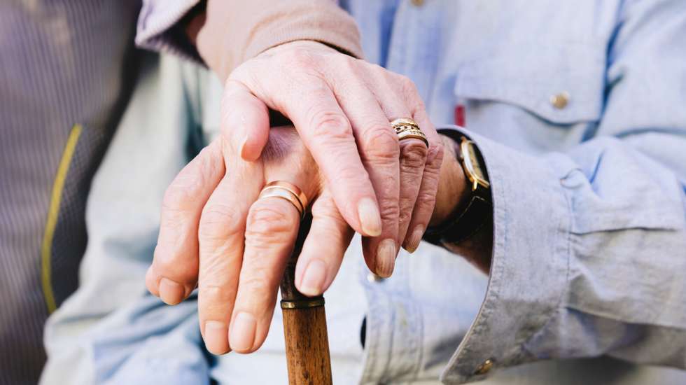 Close-up of old man's and woman's hands resting on a cane