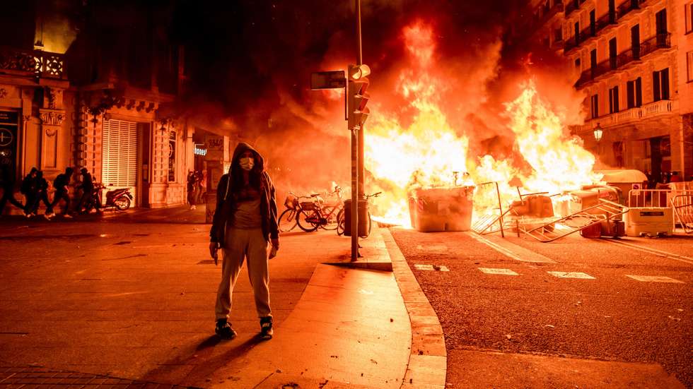 A protester stands in front of burning barricades on Rambla
