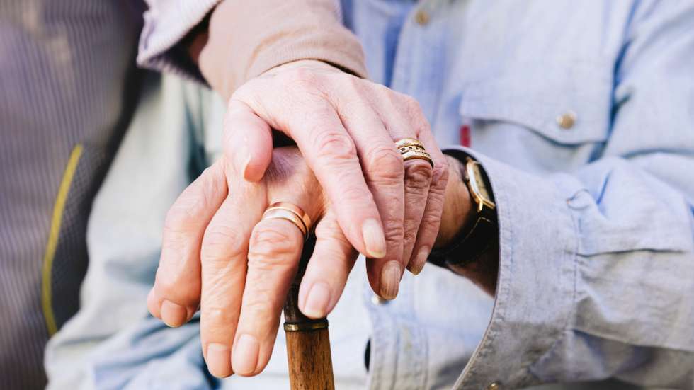 Close-up of old man's and woman's hands resting on a cane