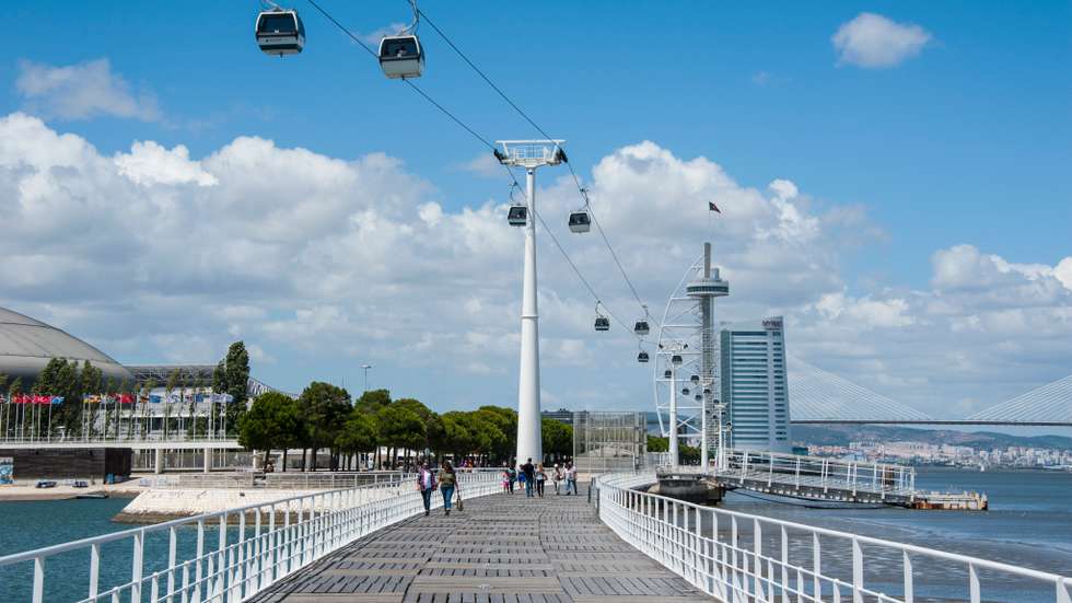 People walking on bridge leading towards Vasco da Gama Tower over river in city against sky, Lisbon, Portugal