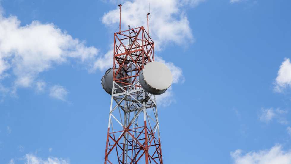 Red and white tower of communications with a lot of different antennas under blue sky and clouds