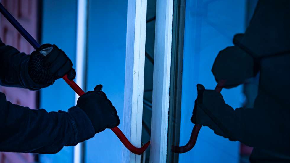 Burglar with crowbar trying break the door to enter the house