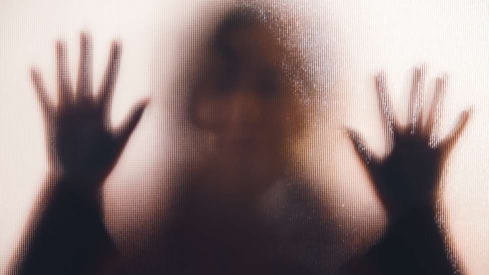 Domestic abuse victim with hands pressed against glass window