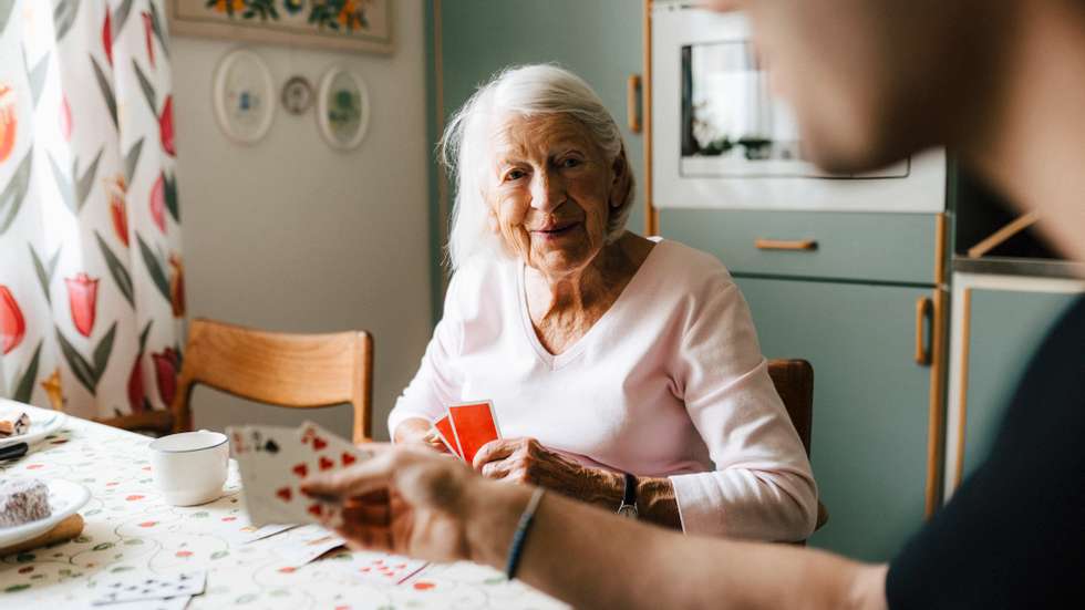 Elderly woman playing cards with male nurse at dining table