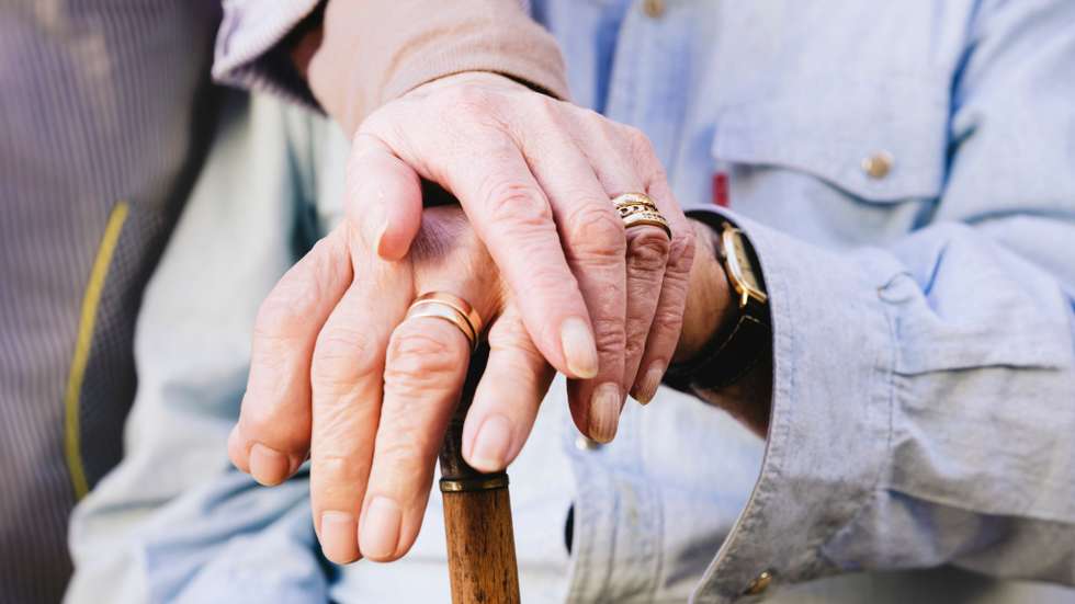 Close-up of old man's and woman's hands resting on a cane