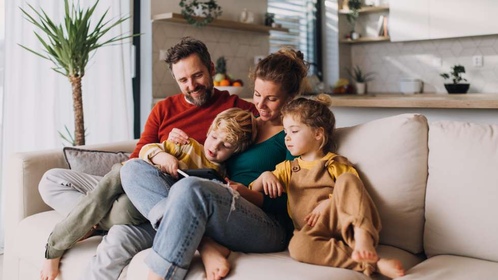 Little children bonding with parents on sofa at home and using tablet.
