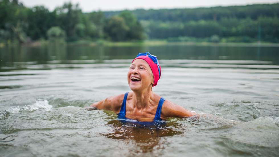 Active senior woman standing in lake outdoors in nature, laughing.