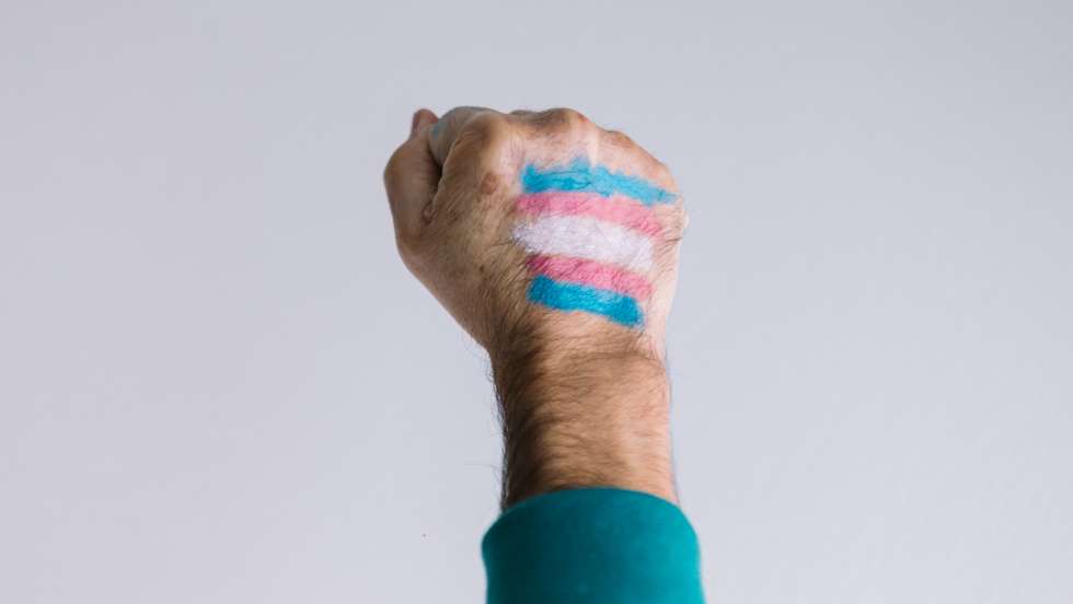 Clenched fist of a man with a painted transsexual flag, wearing an LGTBIQ flag bracelet