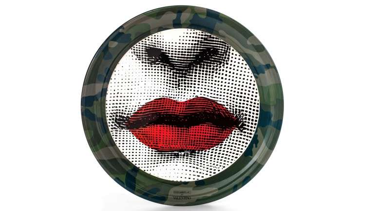 À primeira vista as famosas caras desenhadas por Piero Fornasetti parecem ter-se preparado para a guerra, mas na verdade trata-se de uma colaboração pacífica entre a marca de decoração de luxo e os padrões camuflados da Valentino Garavani. A parceria deu origem a uma coleção da qual fazem parte objetos variados como um banco de madeira, uns óculos escuros e este prato de porcelana (480€), à venda na Farfetch.