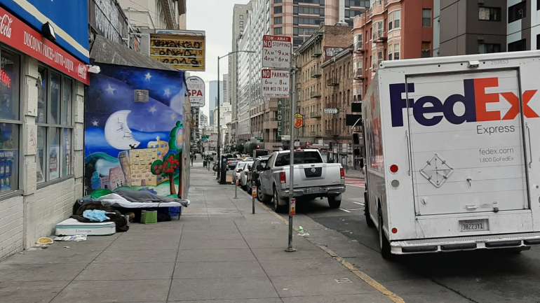 À esquerda, duas pessoas em situação de sem abrigo dormem ao pé de uma carrinha da FedEx