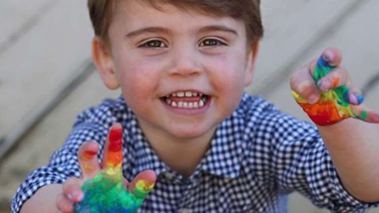 Vestido com uma camisa azul e a sorrir, o príncipe Louis foi fotografado pela sua mãe este mês, em Norfolk, enquanto exibia as mãos pintadas com as cores do arco-íris