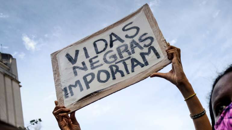 Uma manifestante fazia esvoaçar uma bandeira de Portugal onde estava escrito “o racismo não está a piorar, está a ser filmado”