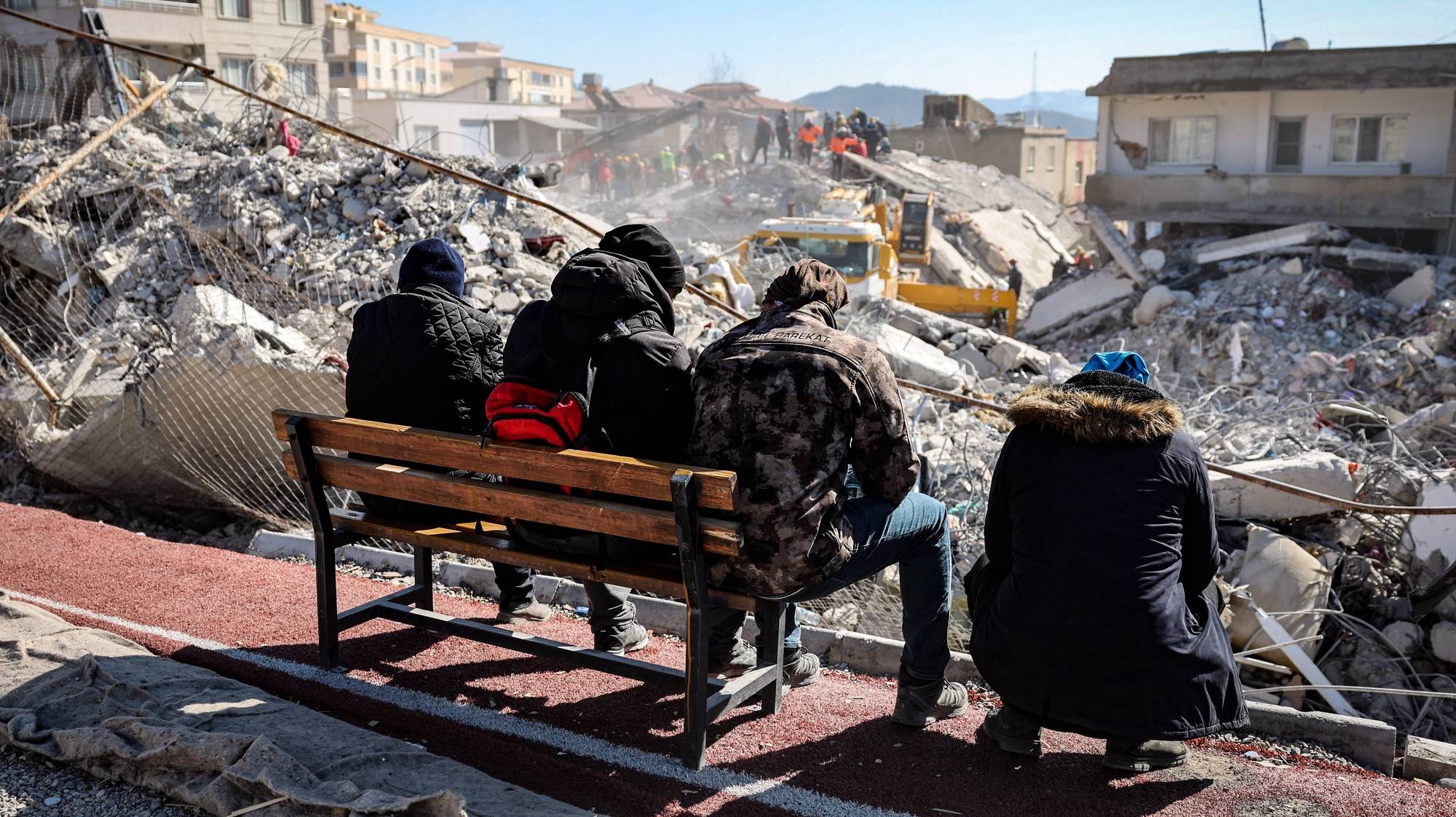 epa10464759 People watch rescue team members work among the rubble of a collapsed building in the aftermath of an earthquake in Nurdagi, southeastern Turkey, 13 February 2023. More than 30,000 people have died and thousands more were injured after two major earthquakes struck southern Turkey and northern Syria on 06 February. Authorities fear the death toll will keep climbing as rescuers look for survivors across the regions.  EPA/JOAO RELVAS