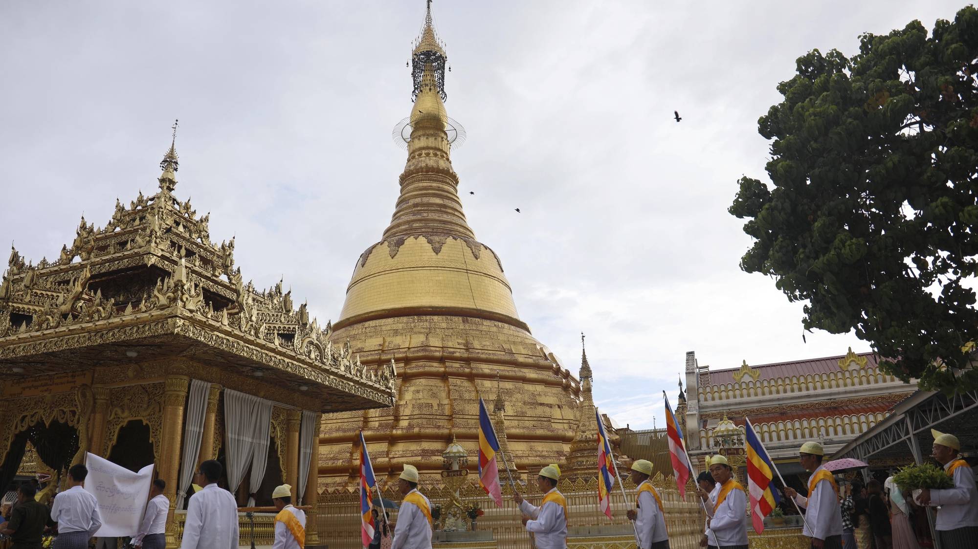 epa11359340 People hold the Buddhist flags as they walk pass on the Botataung pagoda during the full moon day of Kason, the Buddha&#039;s day in Yangon, Myanmar, 22 May 2024. On the Full Moon Day of Kason, Buddhists mark the anniversary of the birth, enlightenment and death of the Buddha.  EPA/NYEIN CHAN NAING