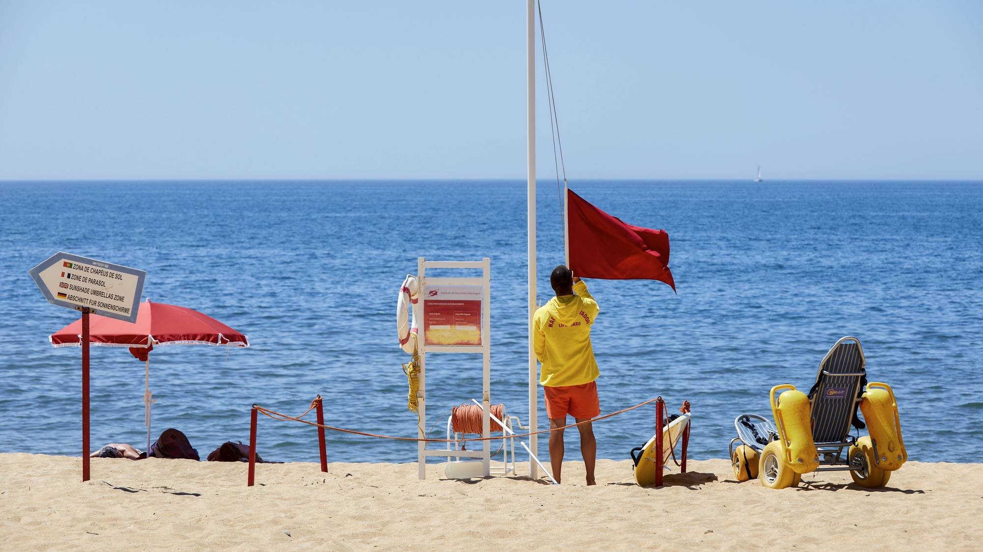 Um nadador-salvador da praia de Quarteira retira a bandeira vermelha, que interditava os turistas a banhos devido à presença de bactérias prejudiciais à saúde na água do mar, para hastear a bandeira verde que permite os banhos, após nova análise à qualidade da água nas praias de Quarteira e Vale do Lobo, em Loulé, 26 de julho de 2023. A interdição a banhos nas praias de Quarteira e Vale do Lobo, no Algarve, que durou menos de 24 horas e cuja interdição foi hoje levantada, foi causada por um foco de poluição. RICARDO NASCIMENTO/LUSA