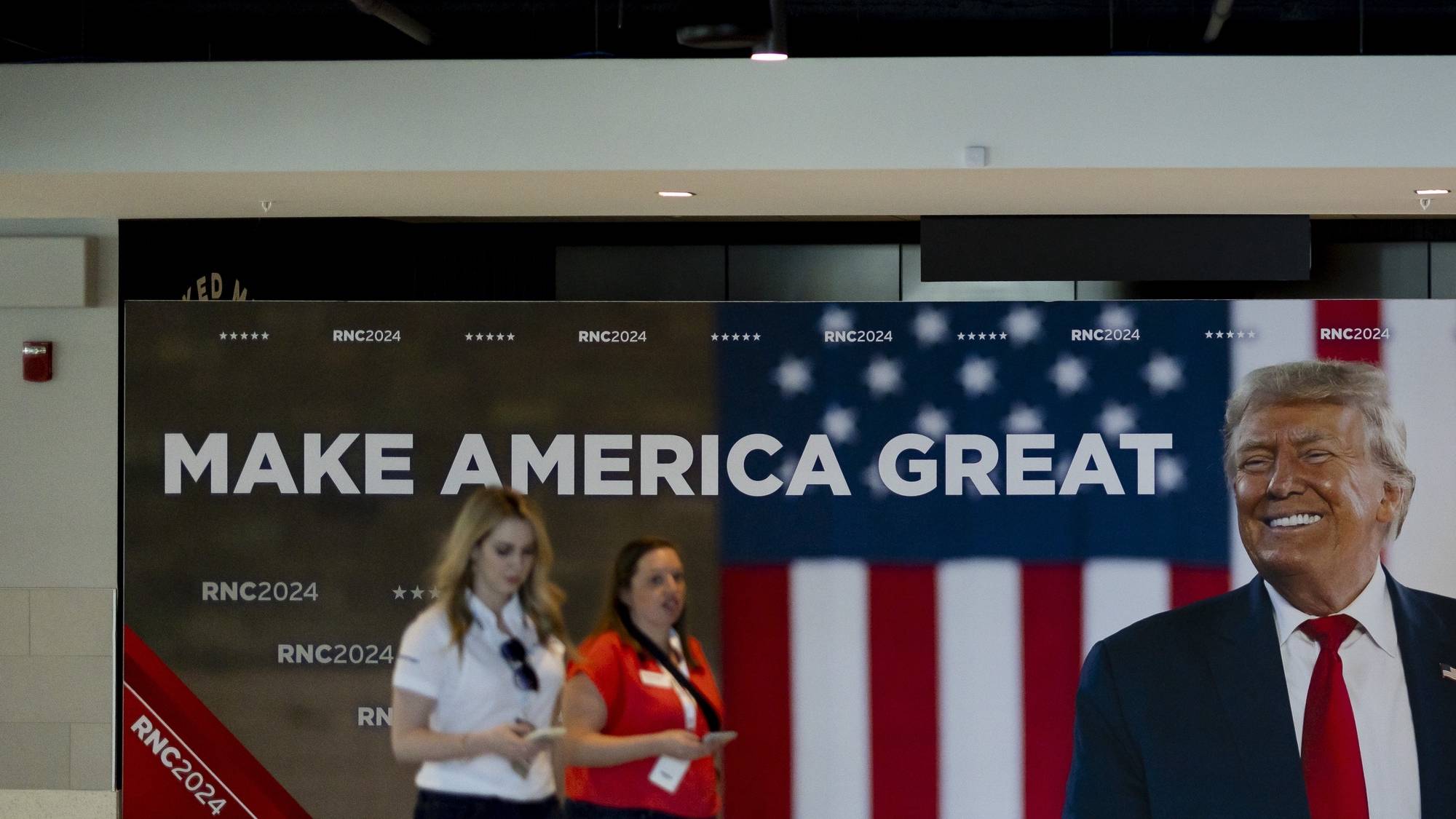 epa11476671 People walk past a picture of former US President J. Trump in the hallways during preparations for the Republican National Convention inside Fiserv Forum in Milwaukee, Wisconsin, USA, 13 July 2024. Republicans will gather for their convention starting on 15 July and will officially confirm Donald J. Trump as the party’s candidate for President of the United States.  EPA/JUSTIN LANE