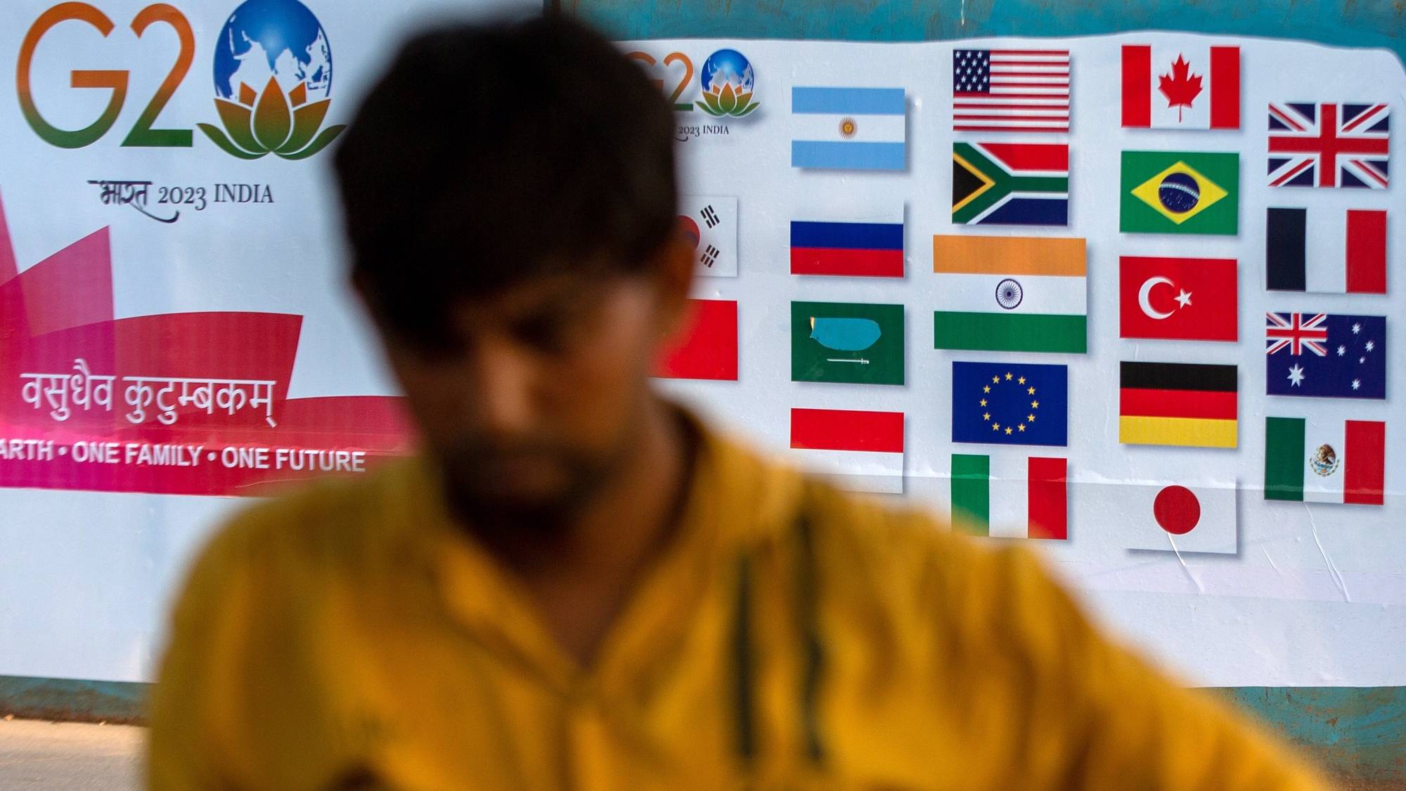 epa10362020 A man stands in front of a G20 poster on a street of Mumbai, India, 12 December 2022. India officially assumed G-20 Presidency on 01 December 2022.  EPA/DIVYAKANT SOLANKI