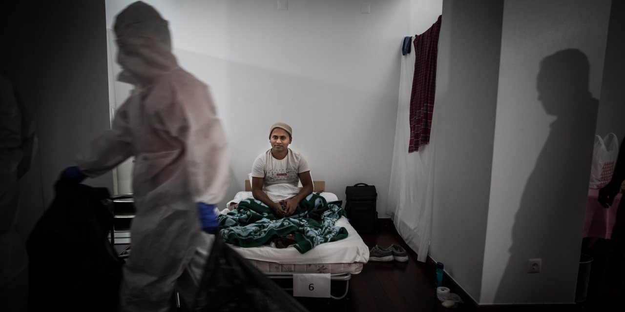 Um dos 14 imigrantes alojados no anexo da mesquita, sentado na sua cama. À esquerda, um dos bombeiros que monitoriza o seu estado de saúde. Nem todos os migrantes aceitaram ser fotografados