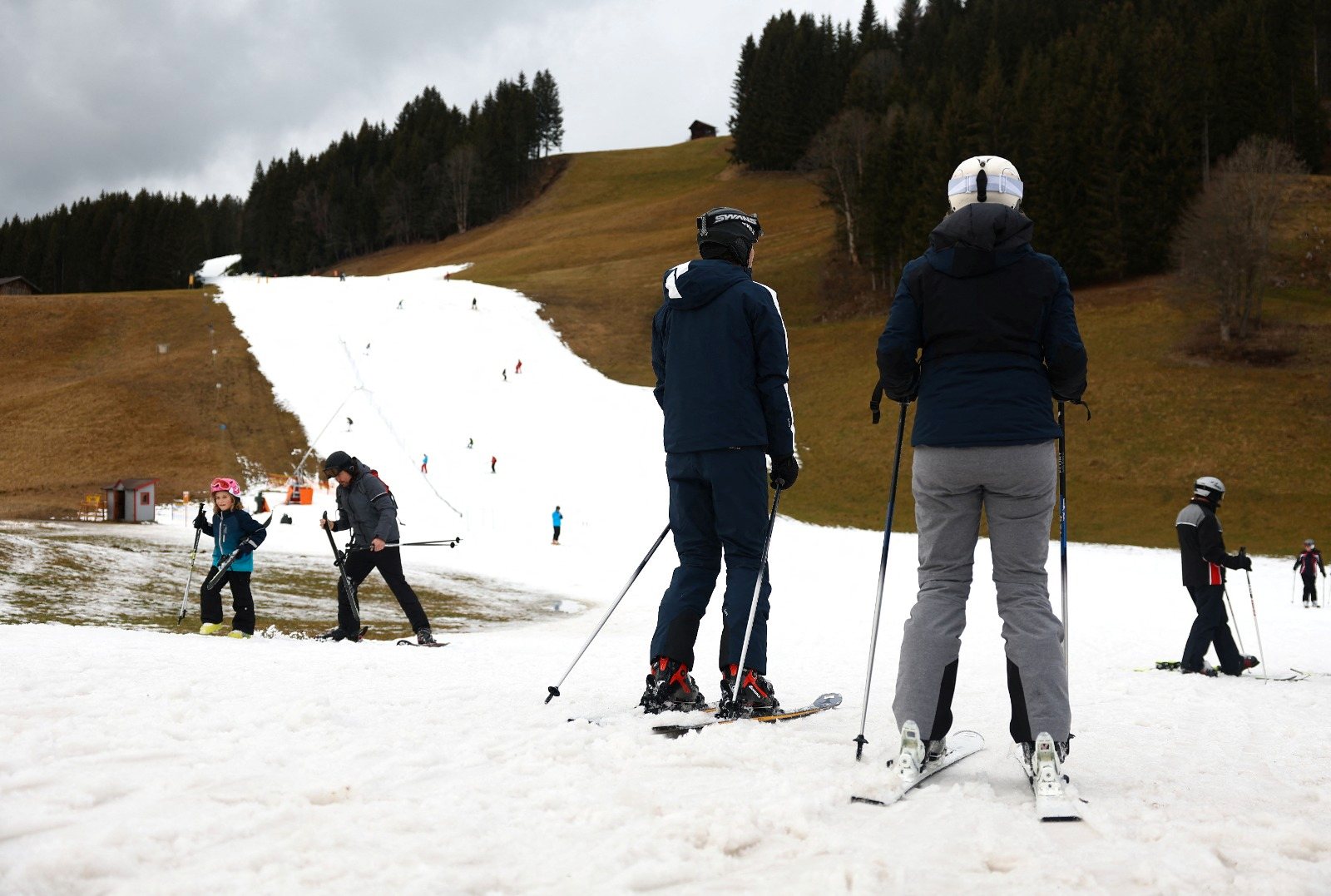 Skiers pass on a small layer of an artificial snow slope between grassland amid warmer-than-usual winter temperatures in the Alps in Filzmoos, Austria, January 5, 2023. REUTERS/Lisi Niesner
