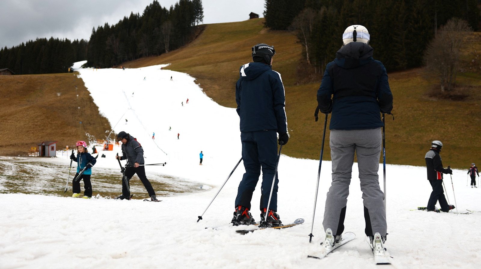 Skiers pass on a small layer of an artificial snow slope between grassland amid warmer-than-usual winter temperatures in the Alps in Filzmoos, Austria, January 5, 2023. REUTERS/Lisi Niesner