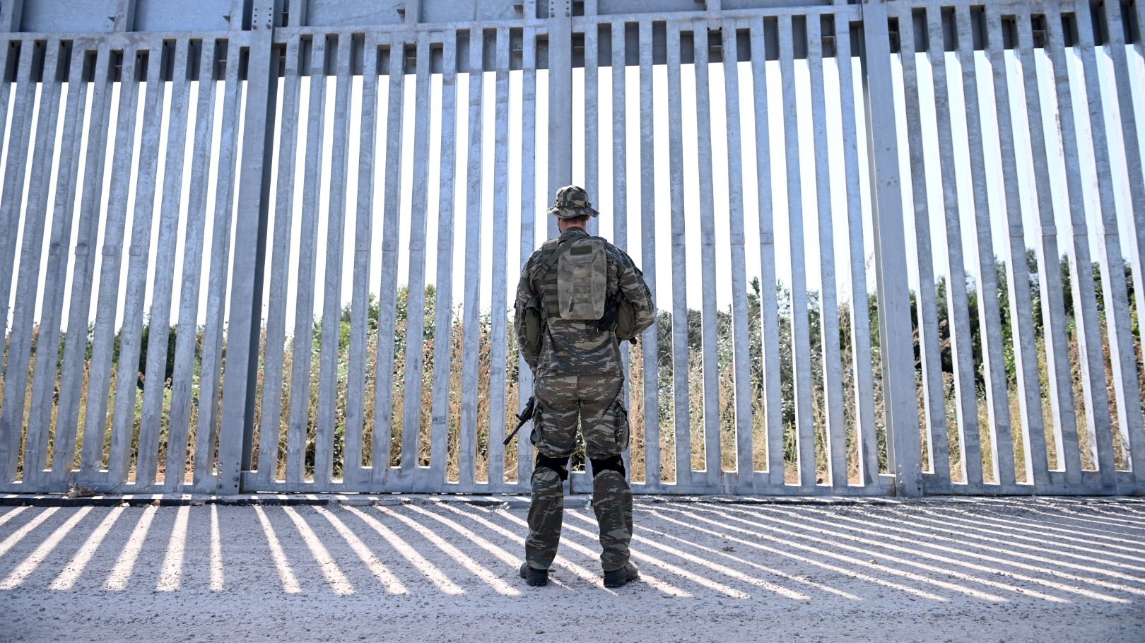 epa09440121 A soldier stands in front of a steel fence built along the Evros River in the area of Feres, at the Greek-Turkish border, Greece, 01 September 2021. The fence was built to prevent the illegal arrival of migrants into Greek territory.  EPA/DIMITRIS ALEXOUDIS