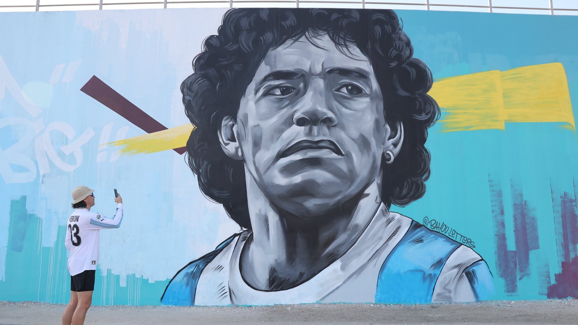 epa10351885 A fan of Argentina takes a picture of a mural depicting Argentinian soccer legend Diego Armando Maradona outside the Khalifa International Stadium in Doha, Qatar, 06 December 2022. Argentina will face the Netherlands in their FIFA World Cup 2022 quarter final soccer match on 09 December 2022.  EPA/ABIR SULTAN