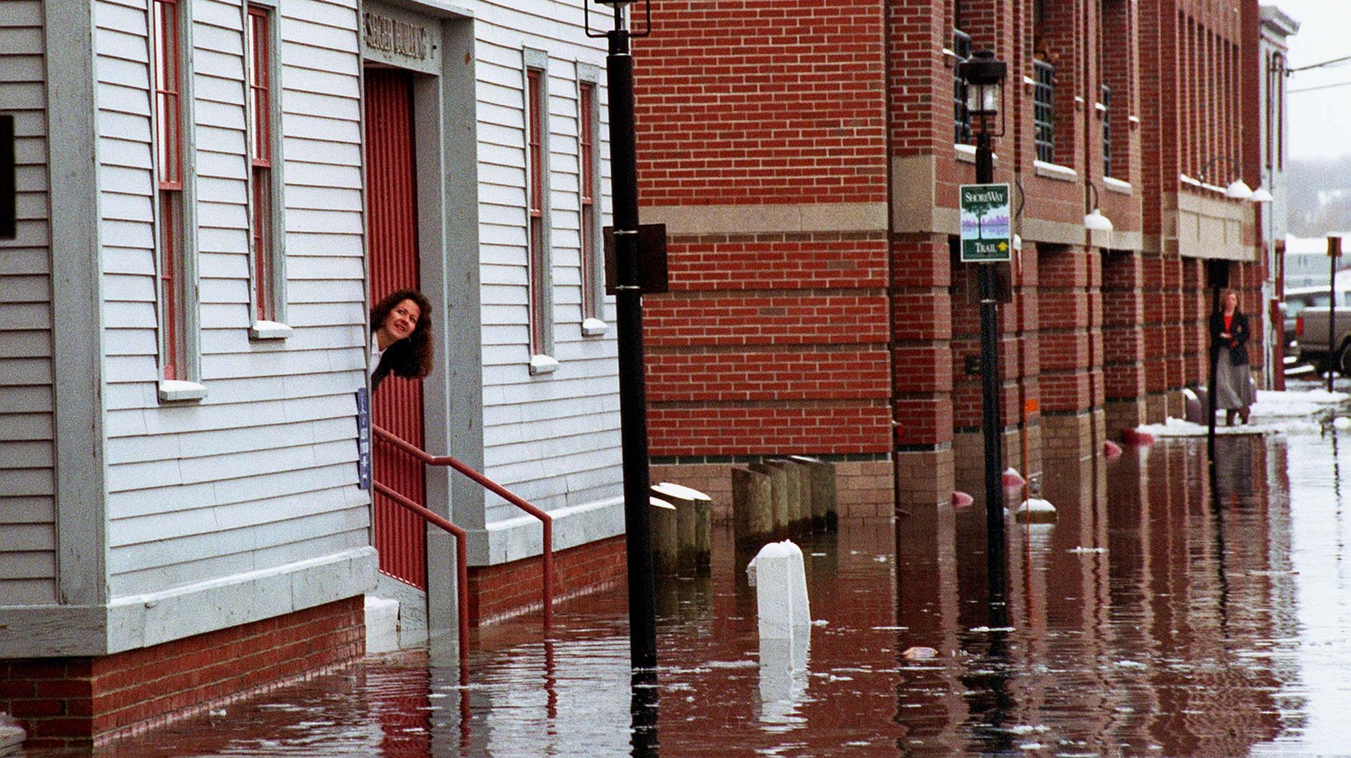 A worker peaks out the door from the Seiger Bldg. on the flooded roadway that connects Portland Pier
