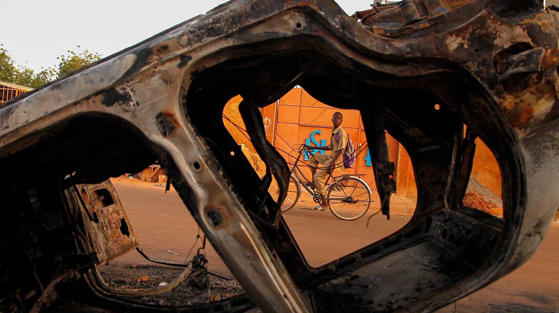 epaselect epa04474287 A boy from Burkina Faso cycles past burned vehicles damaged during violent demonstrations by pro democracy protesters that led to the resignation of President Blaise Compaore in Ouagadougou, Burkina Faso, 03 November 2014. President Blaise Compaore resigned on 31 October 2014 following the violent protests against his bid to change the constitution to extend his rule of 27 years. After a brief claim to power by army General Honore Traore a power struggle ensued with Presidential guard commander Lieutenat-Colonel Isaac Zide being appointed as transitional leader. Thousands of protesters took to the Place de la Nation on 02 November in protest against the military rule.  EPA/LEGNAN KOULA