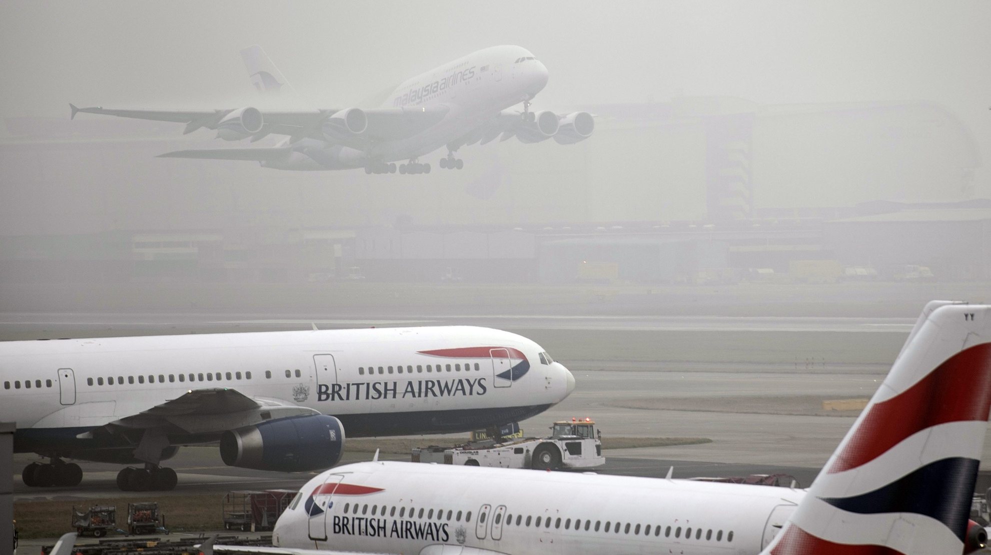 epa05744245 Planes of the British Airways airline gather on the runway as a plane of Malaysia Airlines takes off during thick fog delays departures from Terminal 5 Heathrow Airport in London, Britain, 23 January 2017. Freezing foggy weather threatens to disrupt traffic and travel plans as thick fog saw 100 flights cancelled at Heathrow.  EPA/WILL OLIVER