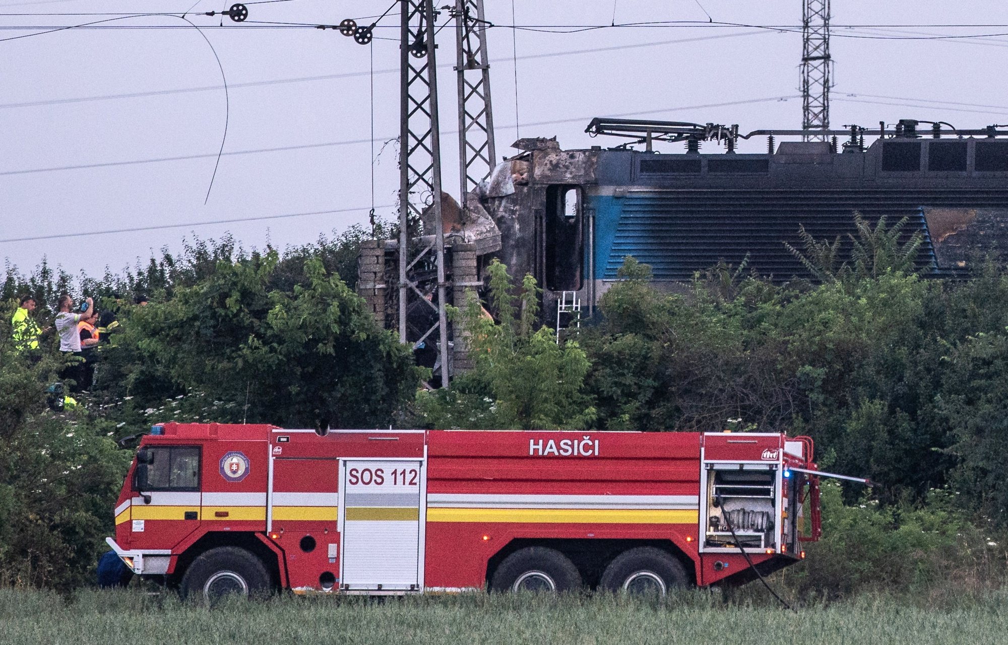 epa11442080 A fire engine stands at the scene in the aftermath of a train crash in the city of Nove Zamky, Slovakia, 27 June 2024. The accident happened at a railway crossing near the town of Nove Zamky in Southern Slovakia. Five ambulances and two helicopters have been despatched to the accident site. An express train carrying more than 100 passengers from Budapest to Prague crashed into a bus shortly after 5 p.m. local time, killing at least five people and injuring several others.  EPA/JAKUB GAVLAK