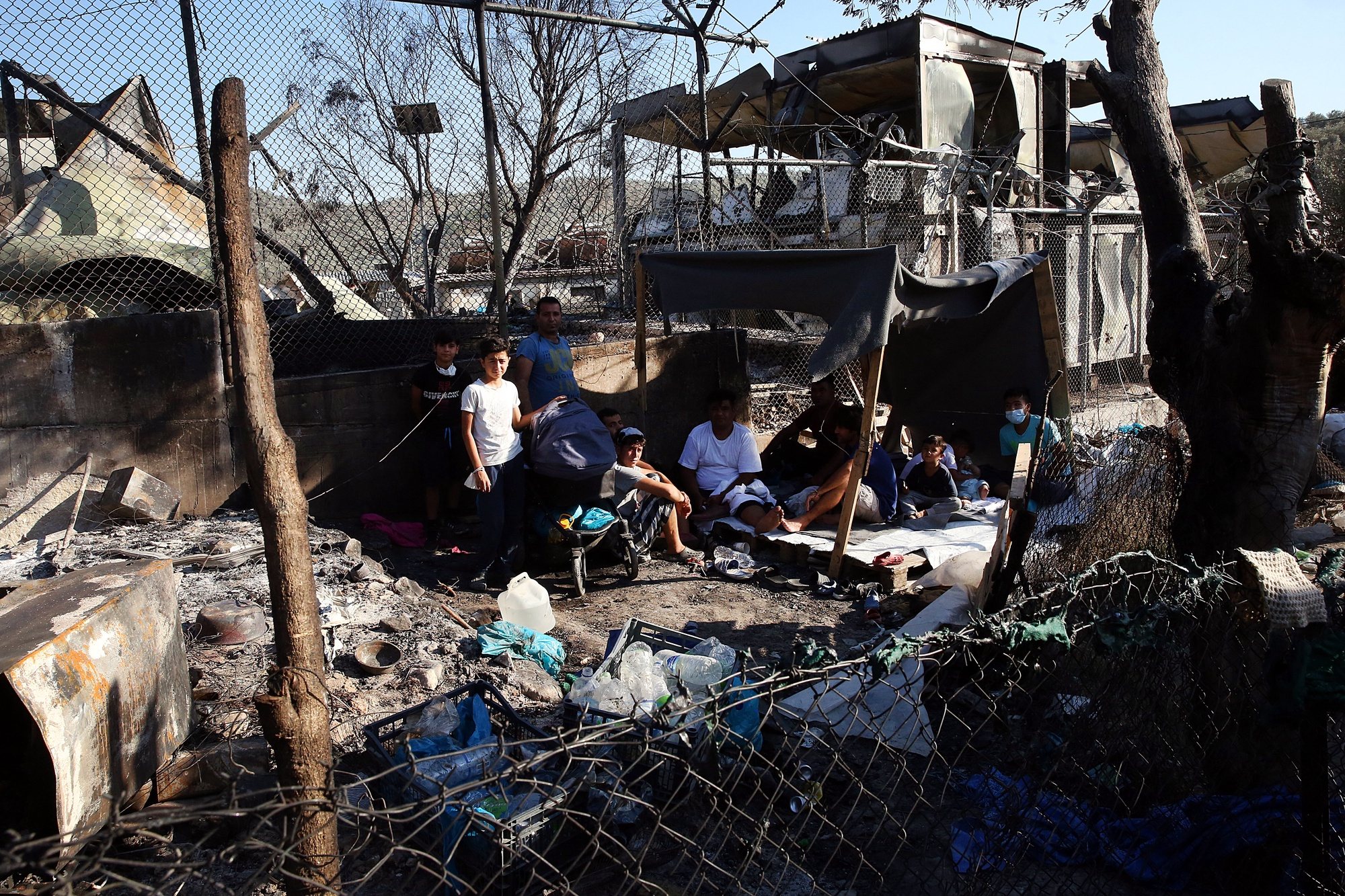 epa08656945 Asylum seekers sit among debris in the Moria refugees camp on the island of Lesbos, Greece, 09 September 2020. According to reports, a fire broke out at Moria Camp early on 09 September, after approximately 35 refugees, who had tested positive for COVID-19, refused to move into isolation with their families.  EPA/ORESTIS PANAGIOTOU