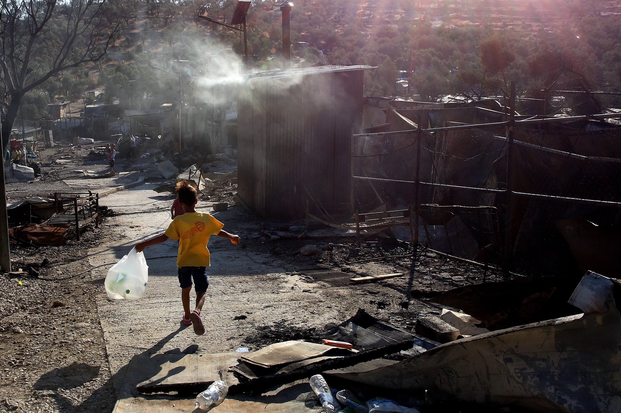 epa08656982 A child walks among debris in the Moria refugees camp on the island of Lesbos, Greece, 09 September 2020. According to reports, a fire broke out at Moria Camp early on 09 September, after approximately 35 refugees, who had tested positive for COVID-19, refused to move into isolation with their families.  EPA/ORESTIS PANAGIOTOU