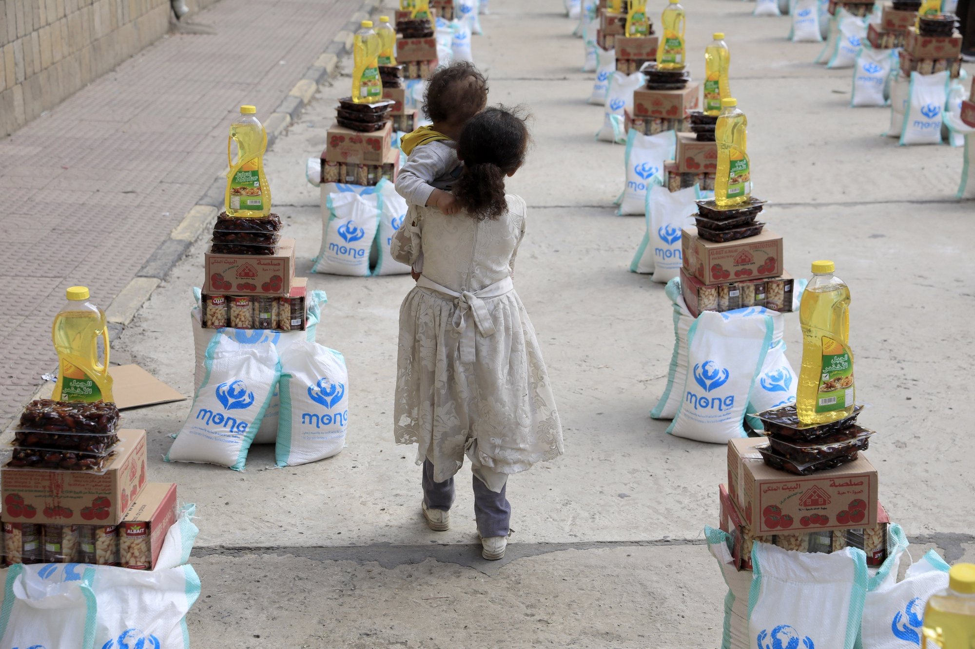 epa11220967 A girl carrying her brother walks amongst food aid provided by Mona relief agency amid acute food insecurity, during the fasting month of Ramadan, in Sana&#039;a, Yemen, 14 March 2024. The Mona relief agency has distributed over 120 food aid baskets to vulnerable families in Sana&#039;a amid acute food insecurity in the war-ravaged country. More than 18 million people in Yemen, over half the population, will need humanitarian assistance and protection services in 2024, according to estimates by the United Nations. The Muslims&#039; holy month of Ramadan is the ninth month in the Islamic calendar, and it is believed that the revelation of the first verse in the Koran was during its last 10 nights. It is celebrated yearly by praying during the night and abstaining from eating, drinking, and sexual acts during the period between sunrise and sunset. It is also a time for socializing, mainly in the evening after breaking the fast, and a shift of all activities to late in the day in most countries.  EPA/YAHYA ARHAB