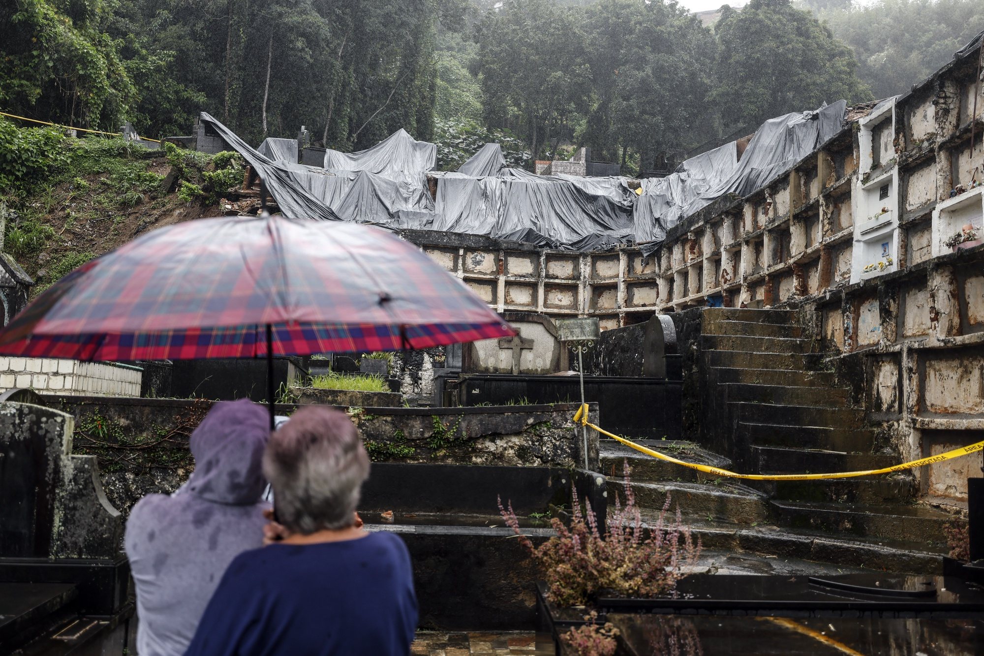 epa11239454 People observe a damaged cemetery caused by the heavy rains in Petropolis, Rio de Janiero state, Brazil, 23 March 2024. At least seven people have died in Rio de Janeiro upon landslides and deluges of water triggered by the heavy rains in the state.  EPA/Antonio Lacerda