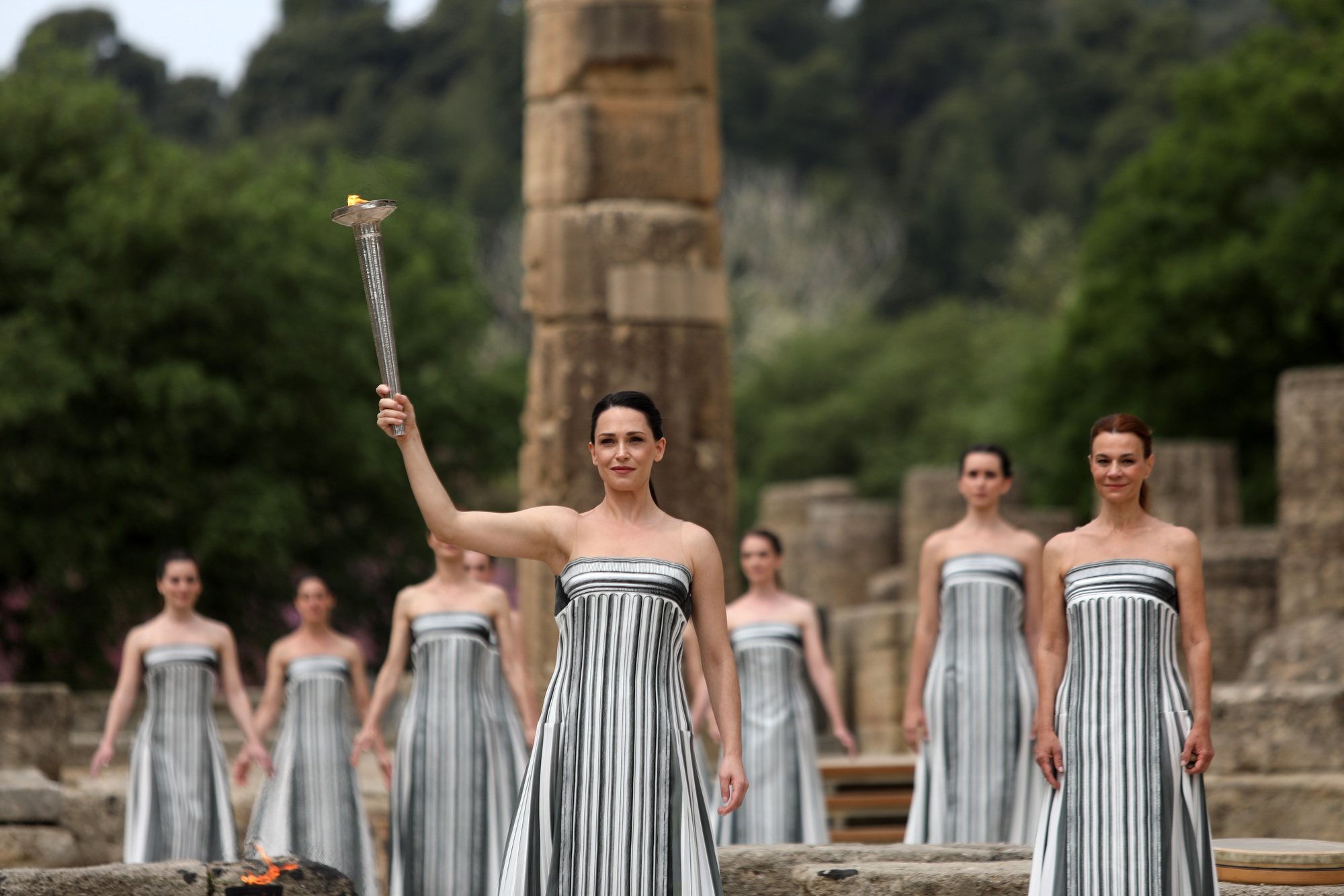 epa11281527 Greek actress Mary Mina, in the role of the High Priestess, raises the torch of the Olympic Flame during the Olympic Flame lighting ceremony for the Paris 2024 Summer Olympic Games, in front of the Hera Temple at the Ancient Olympia site, in southern Greece, 16 April 2024. The Summer Olympics Games will be held in Paris, France from 26 July to 11 August 2024.  EPA/GEORGE VITSARAS