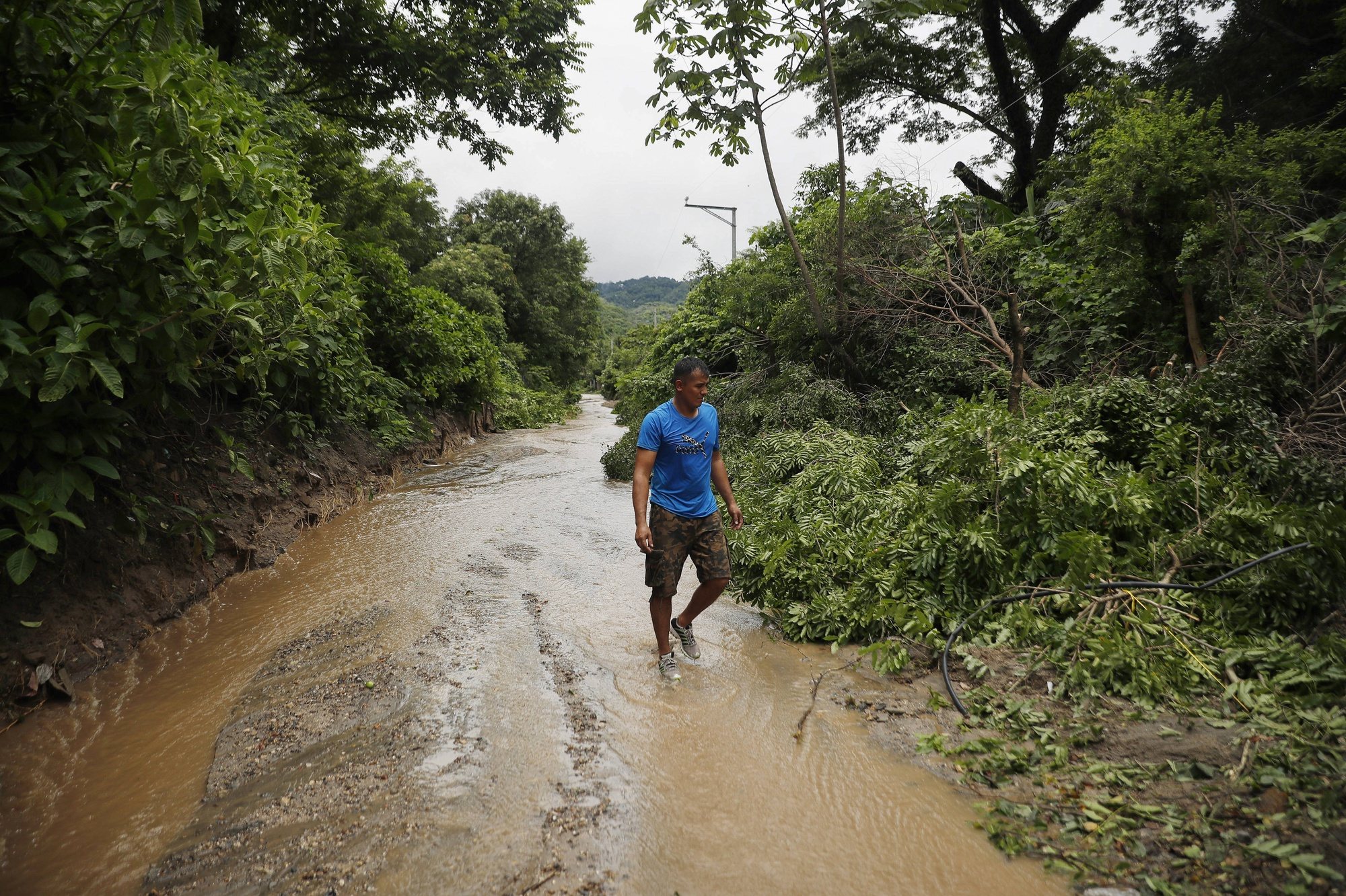 epa11430993 A man walks along a path flooded due to heavy rains in Soyapango, El Salvador, 21 June 2024 (issued 22 June 2024). A Salvadoran family spent the night in a boat after the collapse of an earthen dam destroyed their home and heavy rains threatened more landslides, adding to the more than 3,800 people who have had to be evacuated because of the rains that have lashed El Salvador since last week and have left at least 19 people dead and two missing.  EPA/Rodrigo Sura