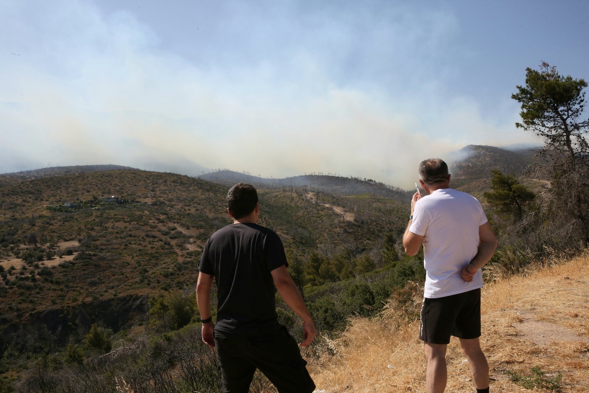 epa11445136 Citizens watch as smoke rises from Mount Parnitha during a wildfire, north Attica, Greece, 29 June 2024. The forest fire started in the location Katsimidi on Mount Parnitha in the afternoon of June 29. Reinforcements were sent in from Thessaly, Epirus and Central Macedonia to help control the fire that is raging on Mount Parnitha, where wind speeds have at times exceeded 100 km per hour, Fire Department spokesperson Vasilis Vathrakogiannis announced during an emergency press briefing.  EPA/ORESTIS PANAGIOTOU