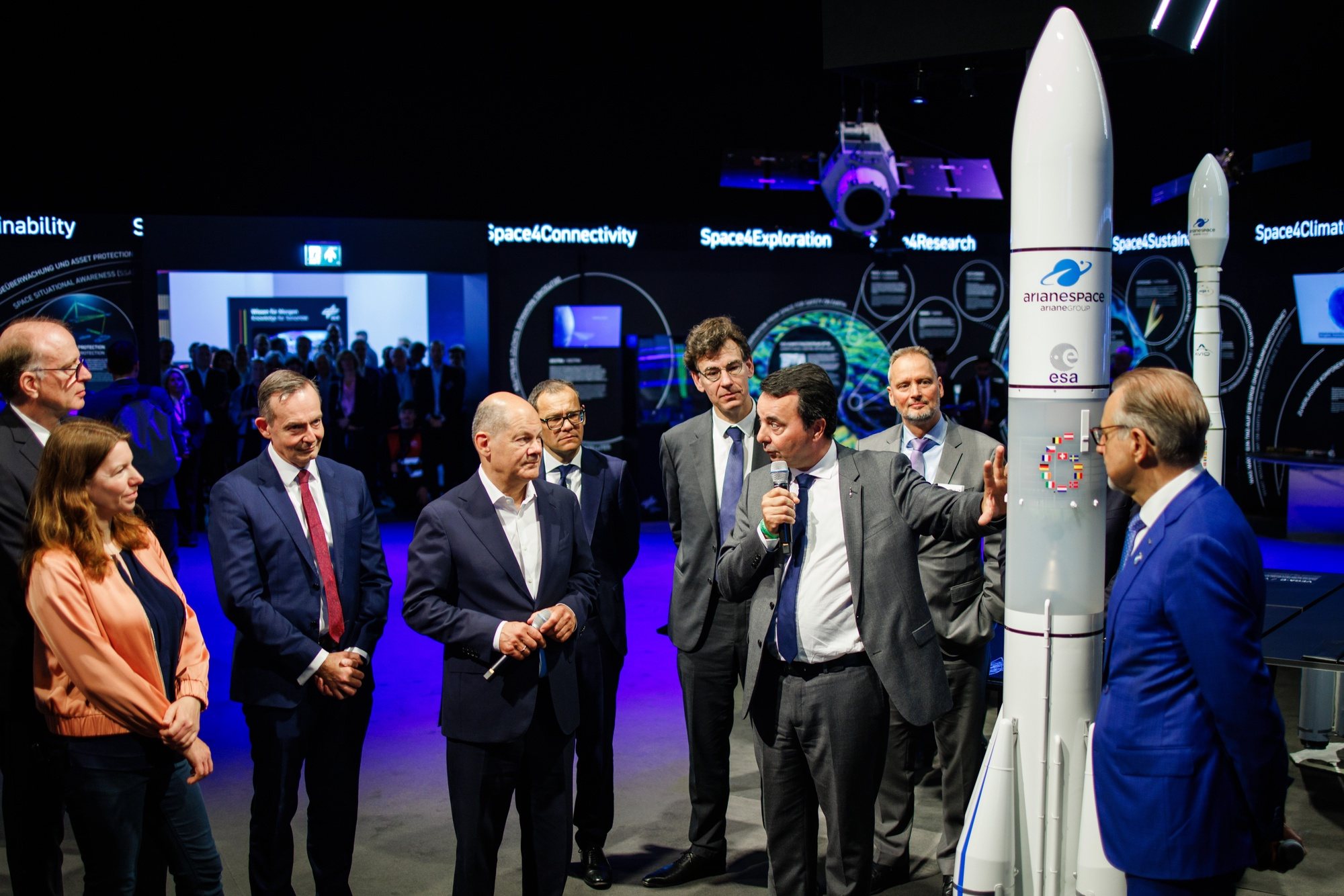 epa11390780 German Chancellor Olaf Scholz (4-L), stands next to German Minister for Transport and Digital Affairs Volker Wissing (3-L) as CEO of ArianeGroup Martin Sion (7-L) talks on front of an Ariane 6 model during the opening round tour of the ILA Berlin Air Show 2024 in Selchow, Germany, 05 June 2024. The aerospace and defense industry exhibition takes place at the inactive Berlin-Brandenburg airport from 05 June to 09 June 2024.  EPA/CLEMENS BILAN