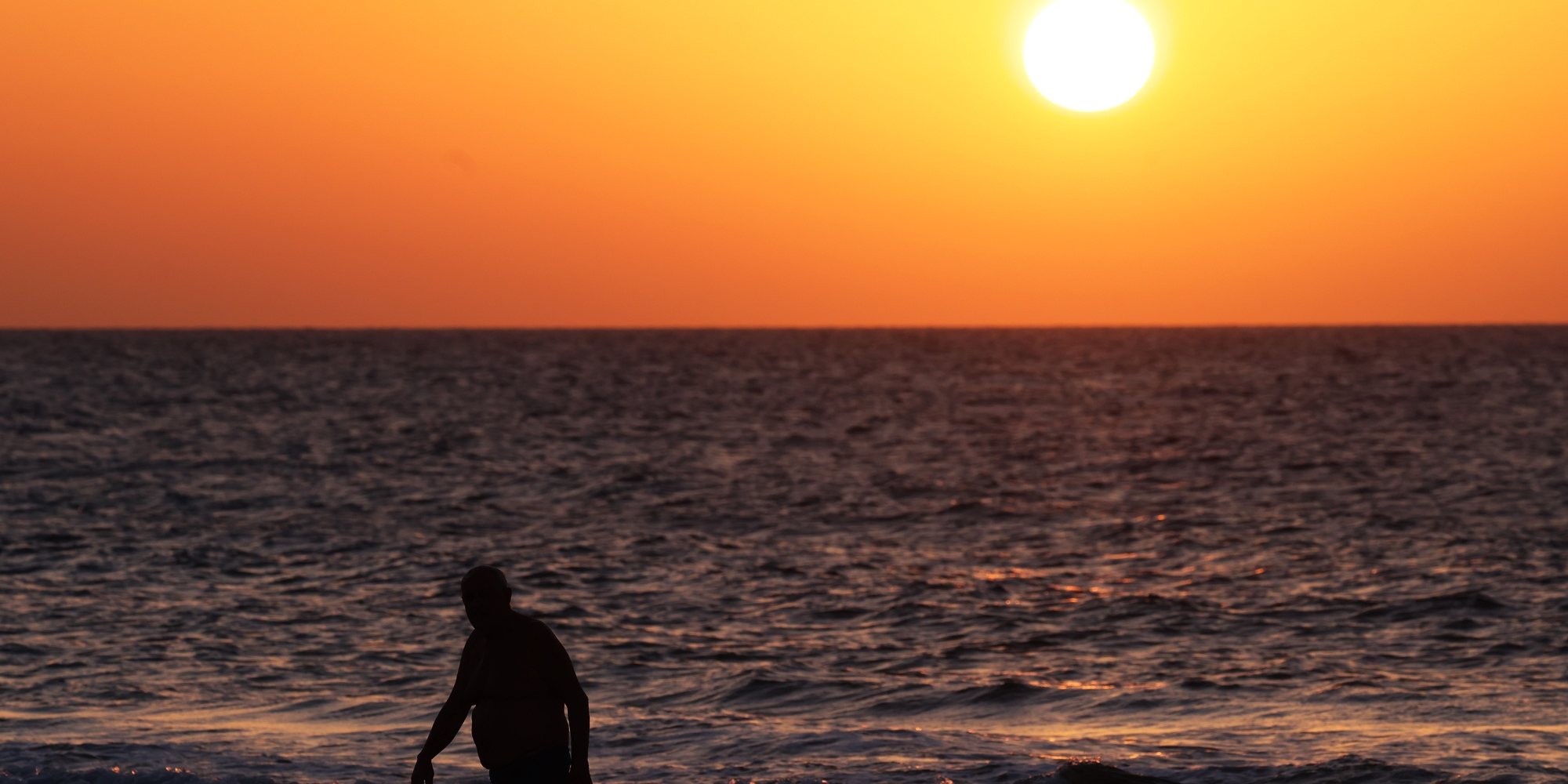 epa10957592 A swimmer exits the sea as the sun sets in Ashdod, Israel, 04 November 2023.  EPA/NEIL HALL