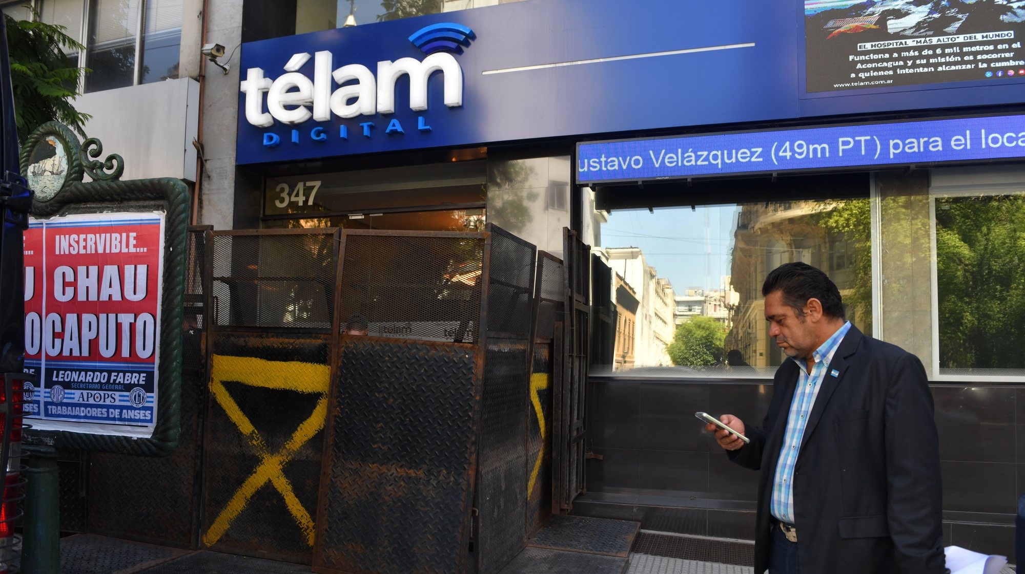 epa11199152 A journalist looks at his cell phone outside the state news agency Telam, whose doors are barricaded, in the San Telmo neighborhood in Buenos Aires, Argentina, 04 March 2024. After the Argentinian President announced the closure of the state news agency Telam, the website appeared as a &quot;page under reconstruction&quot; and the door to the headquarters appeared fenced. The workers gathered in a symbolic &#039;hug&#039; to defend the public media, which, throughout the weekend, received the support of the national and international journalistic world  EPA/ENRIQUE GARCIA MEDINA
