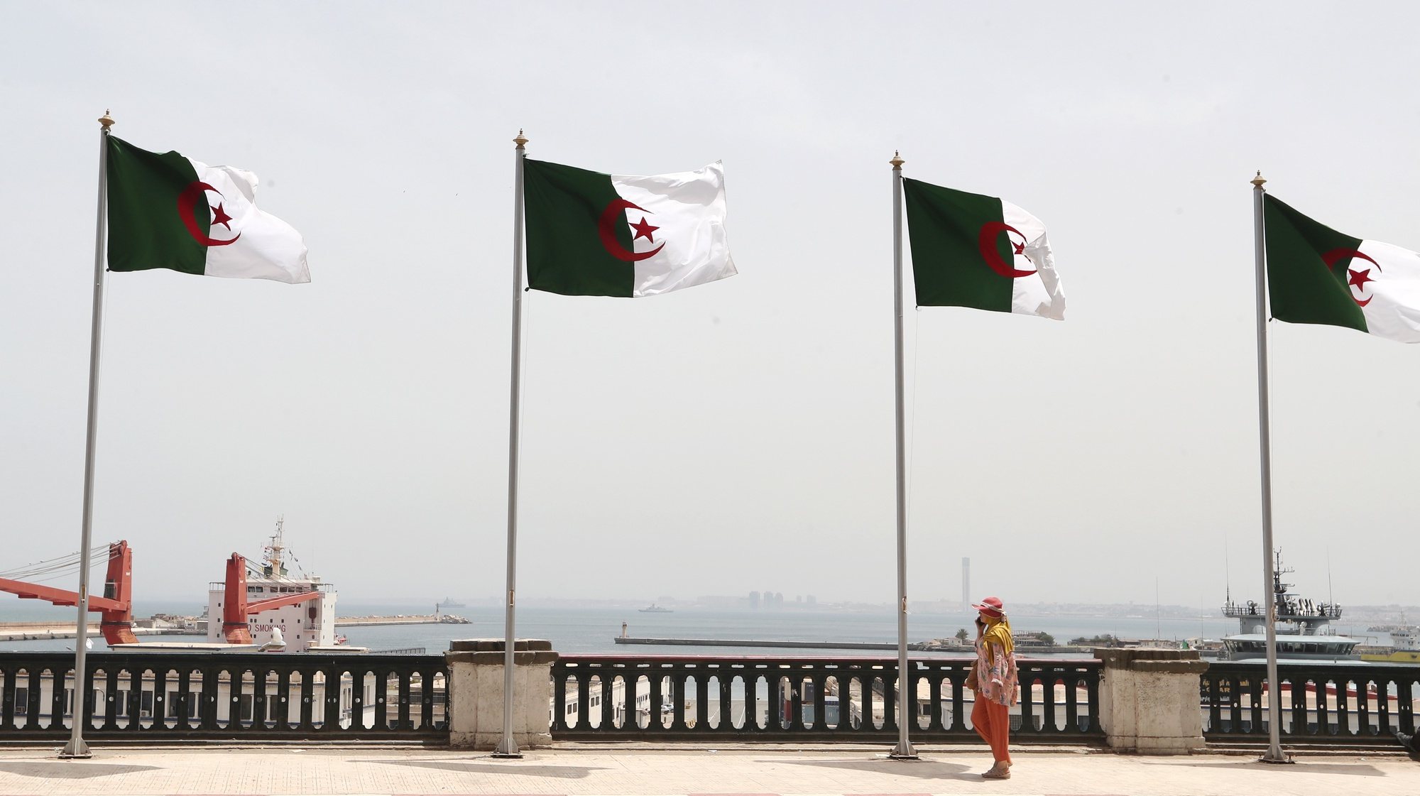epa10052066 A woman walks next to Algerian flags in a street on the eve of celebrations for the 60th anniversary of the Independence, in Algiers, Algeria, 04 July 2022. Algeria on 05 July celebrates the 60th anniversary of its independence from French rule.  EPA/MOHAMED MESSARA