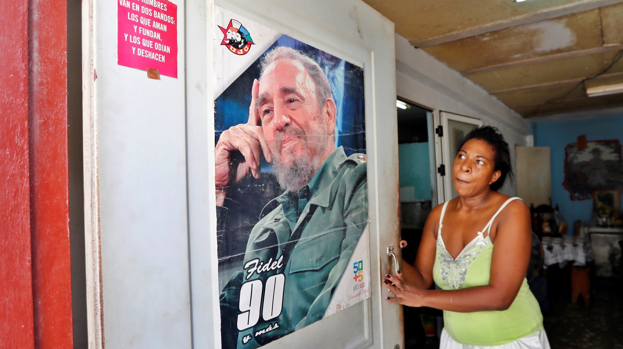 epa09494502 A woman observes a poster with the image of the historical leader of the Cuban revolution Fidel Castro at the door of her house, in Havana, Cuba, 28 September 2021. The Cuban Government commemorates on 28 September the 61st anniversary of the largest mass organization in the country. The CDR (Committees for the Defense of the Revolution) were born in 1960 with the objective of maintaining control and collective surveillance of everything that could destabilize the Cuban political system after the revolution.  EPA/Ernesto Mastrascusa