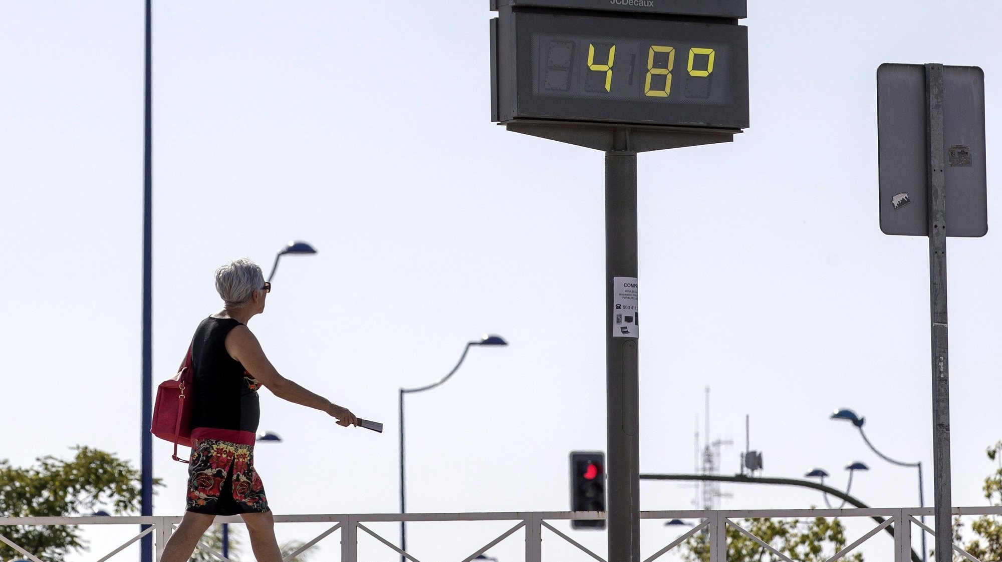 epa06035845 A woman with a fan walks next to a thermometer that marks 48 degrees in Sevilla, Spain, 18 June 2017. Spain is under a heat wave with higher than normal in this time of year temperatures.  EPA/JULIO MUNOZ
